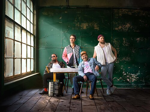 Gankino Circus Auf dem Bild sind die vier Künstler der Band Gankino Circus in eine Art Klassenzimmer zu sehen.