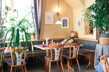 Tische und Stühle eingerahmt von Zimmerpflanzen im hinteren Gastraum der Wallmüller Stuben mit Fensterblick