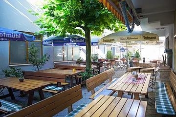 Blick in den Biergarten mit Baum in der Mitte und aufgespannten Sonnenschirmen der beteiligten Brauereien