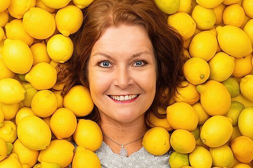 Auf dem Bild ist die Kabarettistin Annette von Bamberg liegend in einem Meer von Zitronen zu sehen.