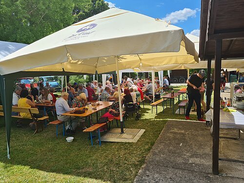 Biertischgarnituren in einer Wiese, mit weißen Sonnenschirmen geschützt.