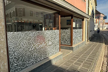 Vor dem Bistro "La Dolce Vita" verläuft ein Gehsteig. Die Schaufenster sind mit einer Klebefolie bis zur Hälfte mit einer gemusterten Folie beklebt.