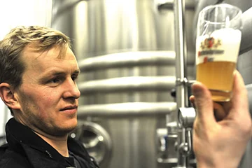 Der Braumeister hält ein Glas mit frisch gebrauten Bier in der rechten Hand und begutachtet es.
