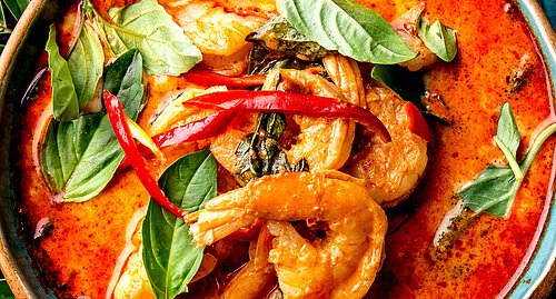 THAI SHRIMPS RED CURRY. Thailand tradition red curry soup with shrimps prawns and coconut milk. Panaeng Curry in blue plate on gray background.