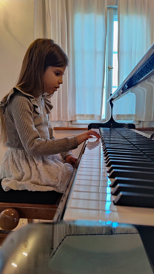 seitliche Nahaufnahme einer jungen Schülerin am Klavier. Sie spielt nur mir der rechten Hand und schaut sehr konzentriert dabei.