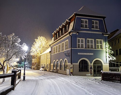 Museum Treuchtlingen_Blaues Haus Zu sehen ist das historische Gebäude Blaues Haus, ein Teil des Museum Treuchtlingen. Es ist Nacht, auf der Straße liegt Schnee und Straßenlaternen erleuchten die Szene.