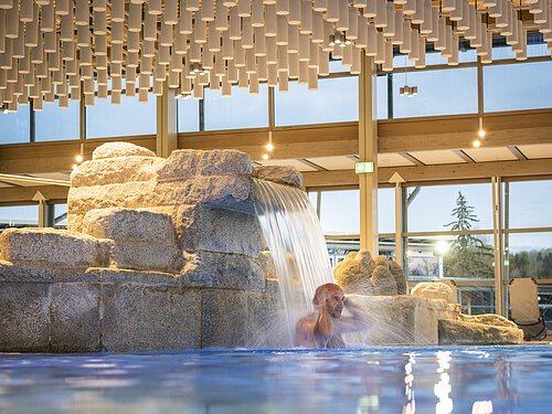 Besucher steht unter dem Wasserfalll im Becken Besucher steht unter dem Wasserfalll im Becken